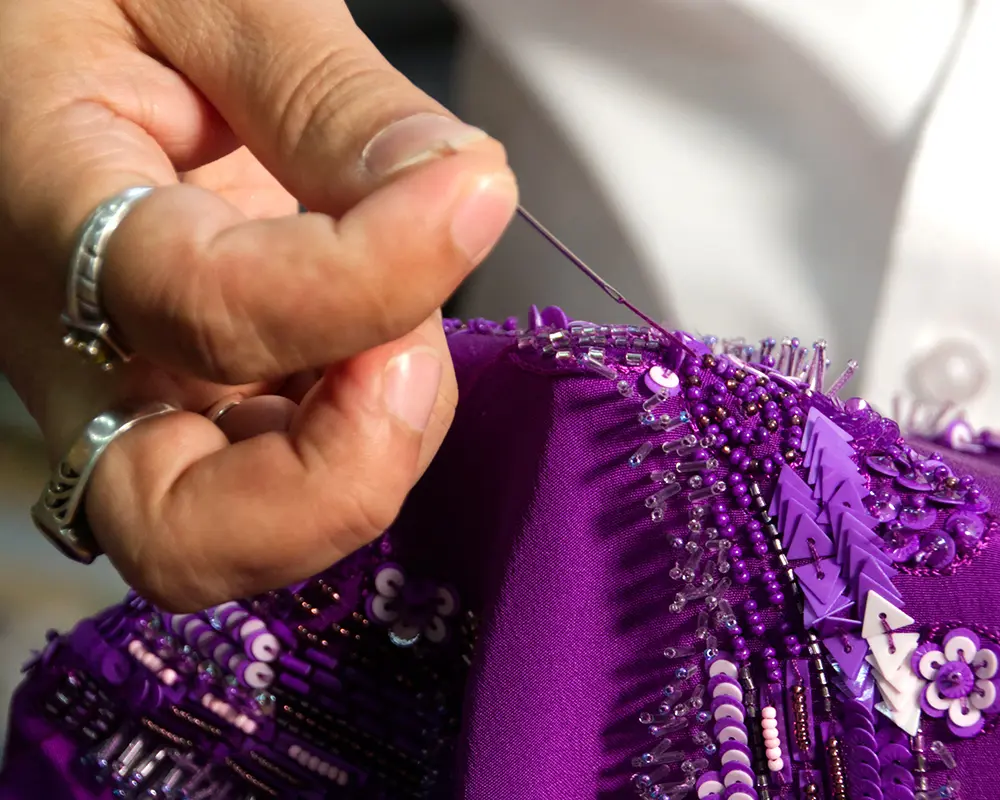 A craftsman at Mrunal Khimji sewing intricate bead work onto purple fabric